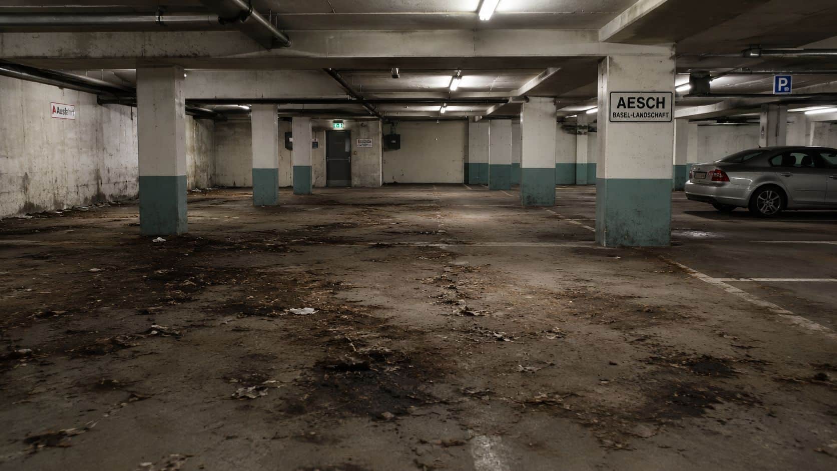 Ein verlassenes, schmutziges Parkhaus in Aesch, Basel-Landschaft mit einem silbernen Auto in der Parklücke.
